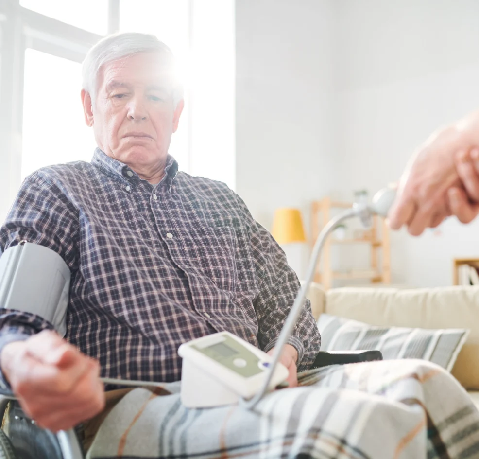 Ein älterer Mann im Rollstuhl der von einer Pflegekraft Blutdruck gemessen bekommt